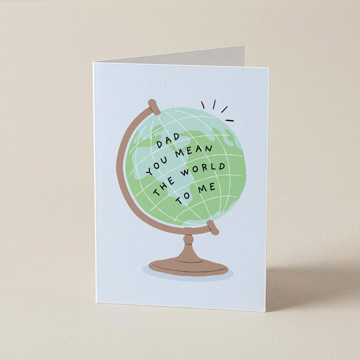 A folded greeting card standing upright on a beige surface. The card features an illustration of a globe with the text 'DAD YOU MEAN THE WORLD TO ME' in black lettering.