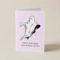 A folded greeting card standing upright on a light beige surface. The card has a pale pink front with a black-and-white ghost illustration and the text 'HAPPY BIRTHDAY YOU SPOOKY BITCH'.