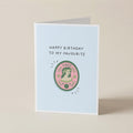 A folded greeting card standing upright on a light beige surface. The card has a pale blue front with the text 'HAPPY BIRTHDAY TO MY FAVOURITE' above a circular illustration featuring a woman's profile and the word 'VIRGO'.