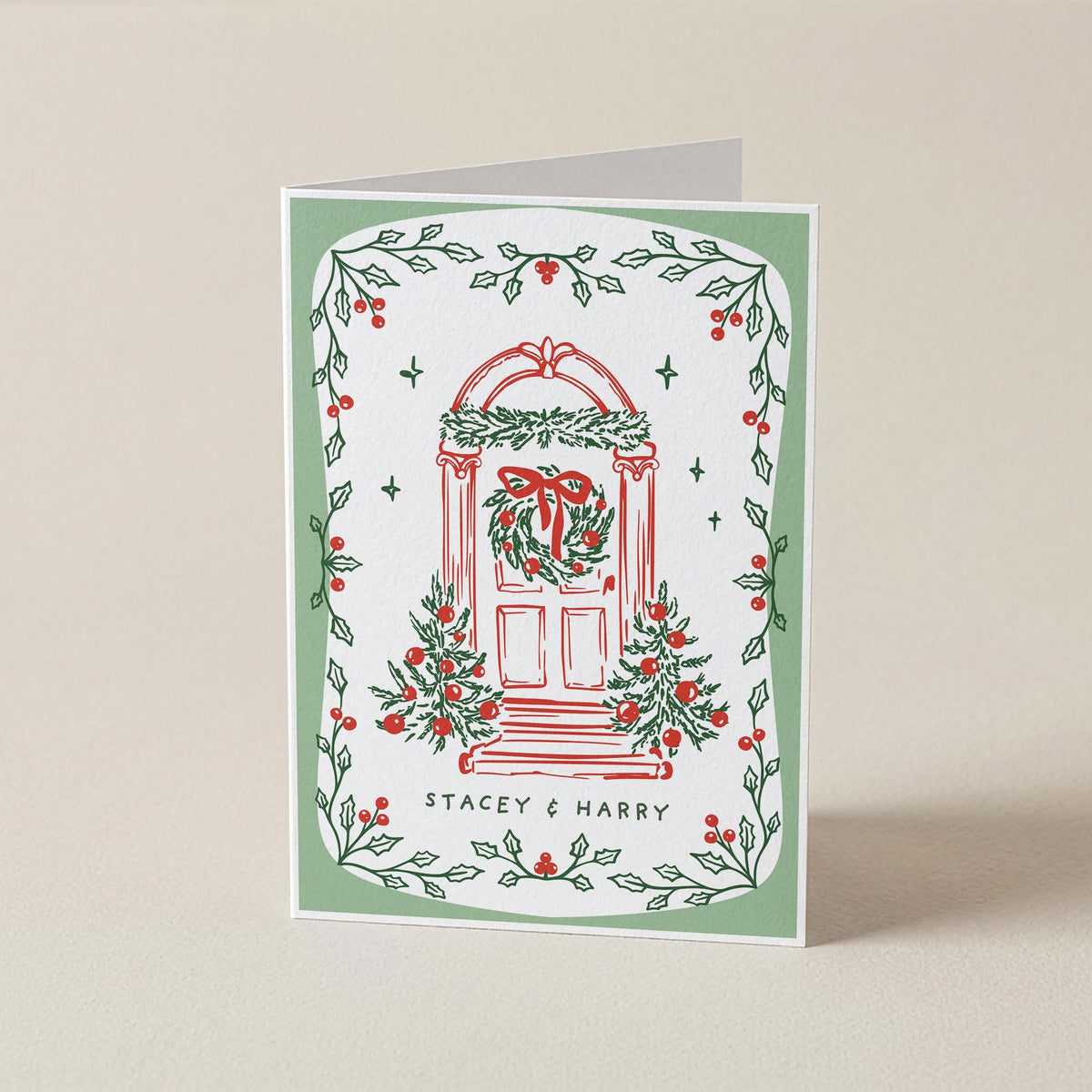 A personalized Christmas greeting card with a white background, featuring a red illustrated door decorated with a green wreath and red bow, surrounded by a border of green holly leaves and red berries. The text 'STACEY & HARRY' is printed at the bottom.