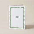 A white greeting card with a light green scalloped border and placeholder text reading 'add your own text here', standing upright on a beige background.