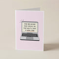 A folded greeting card standing upright on a light beige surface. The card front is pale pink and features an illustration of a laptop with the text, 'SHE BELIEVED SHE COULD, SO SHE QUIT & GOT A NEW JOB!'.