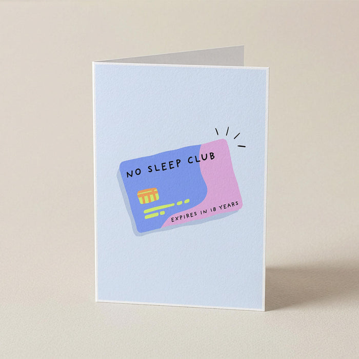 A folded greeting card standing upright on a beige surface, featuring a playful illustration of a credit card that reads 'NO SLEEP CLUB' in black text, with a blue-purple left half and a pink right half.