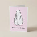 A folded greeting card standing upright on a light beige surface. The card has a pale pink front with a simple black-and-white ghost illustration and the words 'BIRTHDAY GHOUL' printed near the bottom.