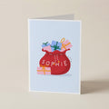 A folded greeting card standing upright on a light beige surface. The card has a pale blue front with an illustration of a red gift sack filled with wrapped presents and the name 'SOPHIE' printed across the sack.