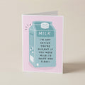 A folded greeting card standing upright on a light beige surface. The card has a pink border and features an illustration of a milk carton in light blue with the text, 'MILK I'M NOT SAYING YOU'RE OLD, BUT IF YOU WERE MILK I'D SNIFF YOU FIRST!'.