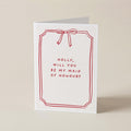 A white greeting card with a red border, red bow illustration, and the text 'HOLLY, WILL YOU BE MY MAID OF HONOUR?' on a light beige background.