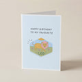 A folded greeting card standing upright on a light beige surface. The card has a pale blue front with the text 'HAPPY BIRTHDAY TO MY FAVOURITE' above a small illustrated lion labeled 'A LEO'.