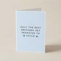A folded greeting card standing upright on a light beige surface. The card is pale blue with the printed message 'ONLY THE BEST BROTHERS GET PROMOTED TO UNCLE!' in black text and two small blue hearts.
