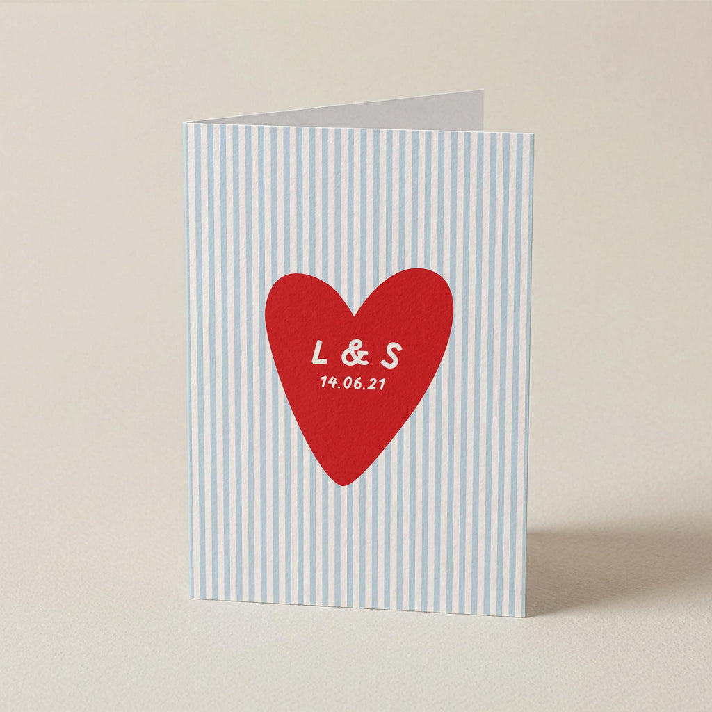 A personalized greeting card with a light blue and white vertical stripe pattern, featuring a red heart in the center with the white printed initials 'L & S' and the date '19.06.