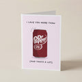 A folded greeting card standing upright on a light beige surface. The card has a pale pink background and features a red Dr. Pepper can.