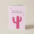 A pink greeting card with a cactus illustration and the text 'YEE HAW, IT'S YOUR BIRTHDAY!' standing upright on a light beige background.
