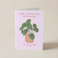 A folded greeting card standing upright on a light beige surface. The card has a pale pink background with an illustration of a green potted plant and the text 'MUM, THANKS FOR HELPING ME' at the top and 'GROW' at the bottom.