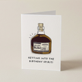 A white greeting card standing upright on a light beige background. The card features an illustration of a bottle of Spiced Rum with the text 'GETTING INTO THE BIRTHDAY SPIRIT!' printed below it.