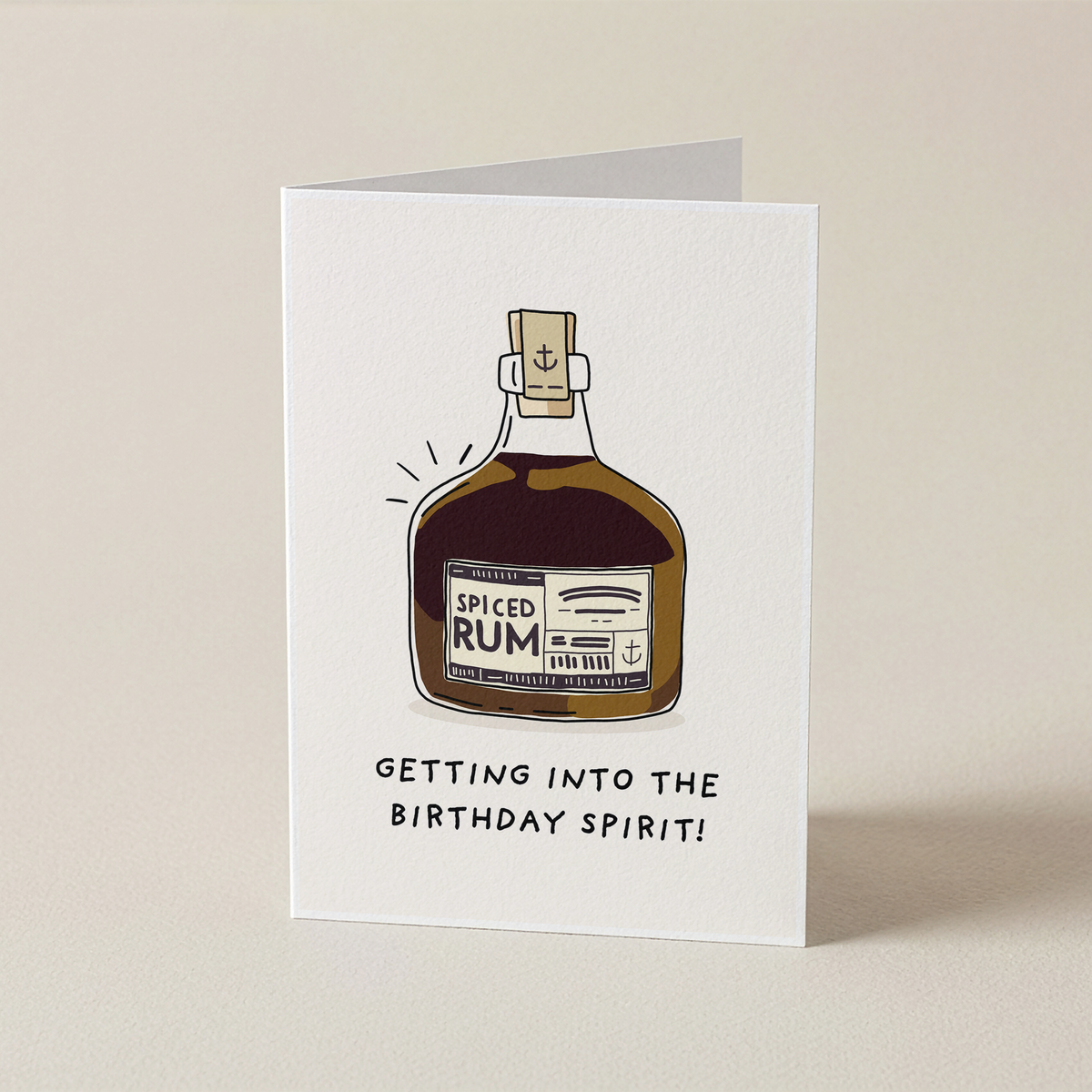 A white greeting card standing upright on a light beige background. The card features an illustration of a bottle of Spiced Rum with the text 'GETTING INTO THE BIRTHDAY SPIRIT!' printed below it.